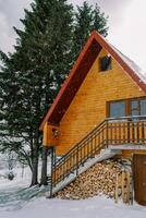 due storie di legno Villetta con un' catasta di legna sotto il passaggi vicino un' abete rosso albero sotto nevicata foto