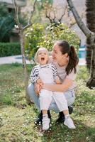 poco ridendo ragazza seduta su sorridente madre giro occupazione nel giardino foto