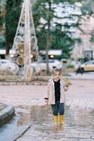 poco ragazza con un' a strisce caramella canna passeggiate attraverso un' pozzanghera nel il parco foto