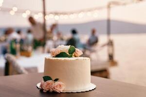 nozze torta sta su il tavolo contro il fondale di ospiti seduta a un' tavolo su il riva del mare foto