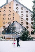 madre con un' piccolo bambino passeggiate di il mano passato un' triangolare Hotel nel il neve. indietro Visualizza foto