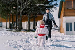 piccolo bambino va per il suo madre in piedi Il prossimo per un' pupazzo di neve nel il cortile. indietro Visualizza foto