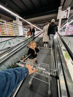 budva, montenegro - 25 dicembre 2022. papà con un' poco ragazza cavalcata un scala mobile nel un' shopping centro commerciale con un' shopping carrello foto