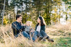 mamma sembra a papà toccante poco figlia naso con il suo dito mentre seduta nel un' radura foto