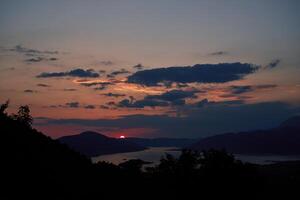 arancia tramonto nel il montagne al di sopra di il baia con buio nuvole su il orizzonte foto