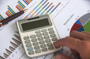 mano urgente calcolatrice con finanziario analisi carta. attività commerciale strategia e bilancio concetto foto