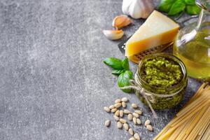 fatti in casa pesto salsa nel piccolo bicchiere vaso e ingredienti per pasta su grigio calcestruzzo sfondo foto