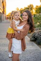 ritratto di mamma e sua poco figlia giocando su città strada esso tramonto luci. alto qualità foto