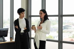 due imprenditrici caucasiche in piedi vicino alla finestra parlando di lavoro in ufficio. concetto di business