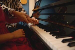 lato Visualizza di un' musica insegnante, musicista pianista Tenere il mani di un' bambino ragazza, insegnamento pianoforte, mostrando il corretta dito posizione. Hobby e tempo libero. bambini formazione scolastica, artistico abilità sviluppo foto