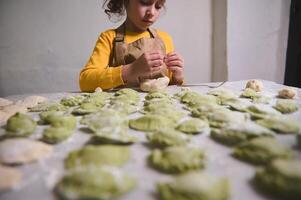 ritratto di un' bello poco casalinga, adorabile bambino ragazza nel dello chef grembiule, cucinando varennyky Ravioli con schiacciato patate, in piedi a cucina tavolo con ingredienti nel rustico accogliente domestico cucina foto