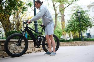 giovane uomo Noleggio equitazione biciclette elettriche nel il città. elettrico bicicletta bicicletta come confortevole ecologico modalità di urbano trasporto foto