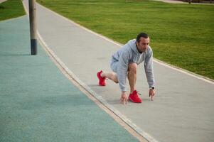 atletico uomo in piedi su un' routine nel Basso di partenza posizione preparazione per sprint nel città parco. attivo persone e sport foto