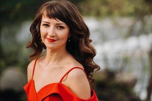 ritratto di un' giovane bellissimo ragazza con lungo Marrone capelli, nel un' lungo rosso vestito nel natura foto