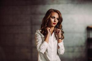 attività commerciale donna nel un' bianca camicia su un' buio studio sfondo.modello con lungo capelli e rosso rossetto foto