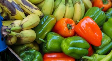 mucchio di dolce verde verde e rosso peperoni e maturo giallo Marrone banane nel scatola di cartone scatola a il strada cibo mercato. fresco frutta e verdure a il contadino cibo negozio. selettivo messa a fuoco. foto