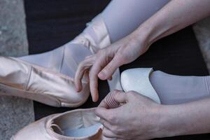 ballerina è mettendo su sua pointe scarpe seduta su il pietra pavimento. balletto ballerino legatura balletto scarpe. danza alunno è preparazione per il prestazione. avvicinamento foto