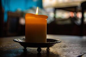 bellissimo candela su il bar tavolo. illuminato candela su il di legno tavolo. ardente candela nel il porta candele. ardente luce. caldo fuoco. accogliente atmosfera. selettivo messa a fuoco. controluce a partire dal il finestra. foto