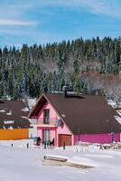 rosa due storie Casa con un' terrazza nel il neve a il bordo di un' conifero foresta nel il villaggio foto