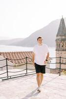 giovane uomo passeggiate lungo il osservazione ponte vicino il campanile di il Chiesa di st. nicola. perasto, montenegro foto