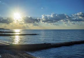 paesaggio marino con sole splendente su una spiaggia di ciottoli foto