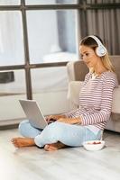 donna bionda caucasica con cuffie e laptop sul divano foto