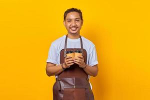 ritratto di un allegro barista che tiene in mano due tazze di caffè di carta tra cui scegliere isolato su sfondo giallo foto