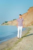 ragazzo in pantaloni bianchi cammina lungo la riva del mare contro foto