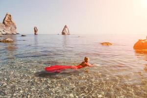 donna viaggio mare. contento turista nel rosso vestito godere assunzione immagine all'aperto per ricordi. donna viaggiatore in posa nel mare spiaggia, circondato di vulcanico montagne, condivisione viaggio avventura viaggio foto