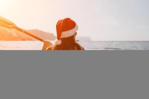 donna nel kayak indietro Visualizza. contento giovane donna nel Santa cappello galleggiante nel kayak su calma mare. estate vacanza vacanza e allegro femmina persone rilassante avendo divertimento su il barca. foto