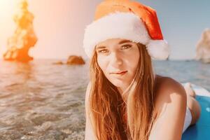 donna mare sup. vicino su ritratto di contento giovane caucasico donna con lungo capelli nel Santa cappello guardare a telecamera e sorridente. carino donna ritratto nel un' bianca bikini in posa su cenare tavola nel il mare foto