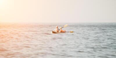 contento coppia kayak nel un gonfiabile kayak su il mare a tramonto. coppia canoa nel il mare vicino il isola con montagne. persone kayak nel vita giacche vela. indietro Visualizza foto