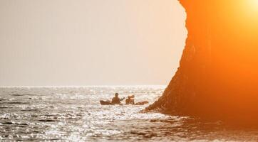 contento coppia kayak nel un gonfiabile kayak su il mare a tramonto. coppia canoa nel il mare vicino il isola con montagne. persone kayak nel vita giacche vela. indietro Visualizza foto