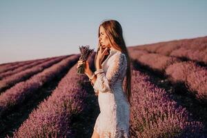 donna lavanda campo. contento spensierato donna nel un' bianca vestito a piedi nel un' lavanda campo e odorare un' lavanda mazzo su tramonto. ideale per caldo e ispirazione concetti nel voglia di girovagare e viaggio. foto