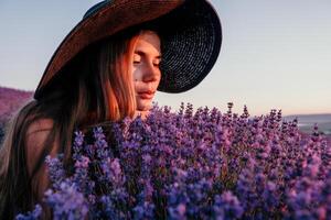 donna lavanda campo. contento spensierato donna nel nero vestito e cappello con grande orlo odorare un' fioritura lavanda su tramonto. Perfetto per ispirazione e caldo concetti nel viaggio e voglia di viaggiare. vicino su foto