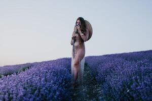 donna lavanda campo. contento spensierato donna nel beige vestito e cappello con grande orlo odorare un' fioritura lavanda su tramonto. Perfetto per ispirazione e caldo concetti nel viaggio e voglia di viaggiare. vicino su foto