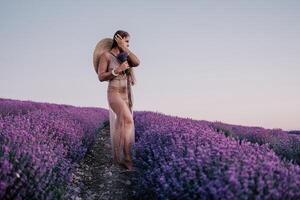 donna lavanda campo. contento spensierato donna nel beige vestito e cappello con grande orlo odorare un' fioritura lavanda su tramonto. Perfetto per ispirazione e caldo concetti nel viaggio e voglia di viaggiare. vicino su foto