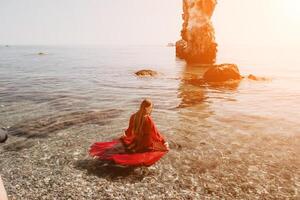 donna viaggio mare. contento turista nel rosso vestito godere assunzione immagine all'aperto per ricordi. donna viaggiatore in posa su il roccia a mare baia circondato di vulcanico montagne, condivisione viaggio avventura viaggio foto