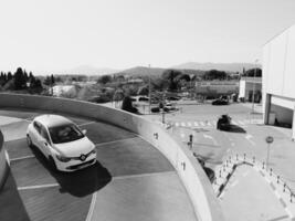 Podgorica, montenegro - 14 agosto 2023. auto unità attraverso il parcheggio lotto di il centro commerciale. nero e bianca foto