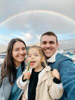 papà, mamma e poco ragazza con lecca-lecca su il sfondo di il arcobaleno al di sopra di il montagne foto