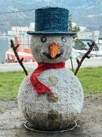 scultura di un' pupazzo di neve nel un' cappello con un' sciarpa sta su il riva del mare foto