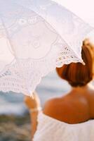 bianca openwork solare ombrello nel il mano di un' donna su il riva del mare foto