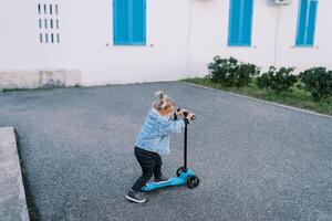 poco ragazza cavalcate un' scooter su un asfalto cortile vicino il Casa foto