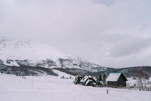 innevato piccolo villaggio dietro a un' di legno recinto a il piede di il montagne foto