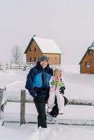 sorridente papà con un' poco ragazza su il suo giro seduta su un' innevato recinto nel il villaggio foto