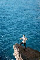 giovane sorridente uomo in piedi su un' pietra ripiano sopra il mare con il suo pollici su foto