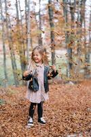 poco ridendo ragazza sta con sua occhi chiuso e sua testa trasformato sotto il caduta asciutto le foglie nel il autunno foresta foto