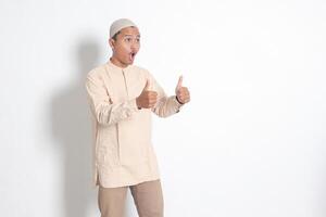 ritratto di attraente asiatico musulmano uomo nel koko camicia mostrando pollice su, bene lavoro mano gesto. approvazione concetto. isolato Immagine su bianca sfondo foto