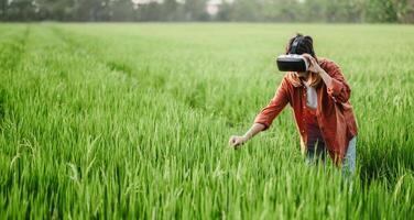 assorto nel un' virtuale la realtà Esperienza, un' donna raggiunge giù per toccare il lussureggiante erba nel un' campo, mescolanza il digitale e naturale mondi. foto