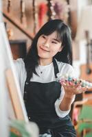 un' giovane donna con un' luminosa Sorridi seleziona vernici a partire dal sua tavolozza, sua occhi scendete con creatività, nel un' accogliente arte studio ambientazione. foto